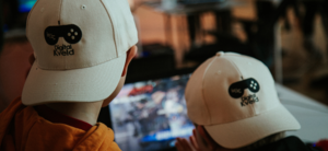 To barn spiller dataspill. De har på seg beige caps med logoen Digital Kveld på. Fotografi.